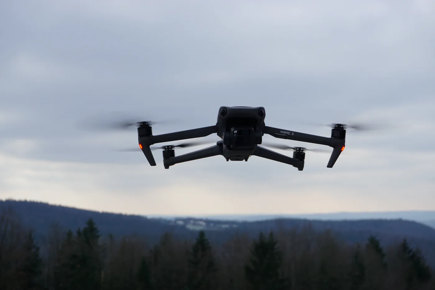 DJI Mavic 3 mit Hasselblad-Kamera im Schwebeflug vor Waldkulisse